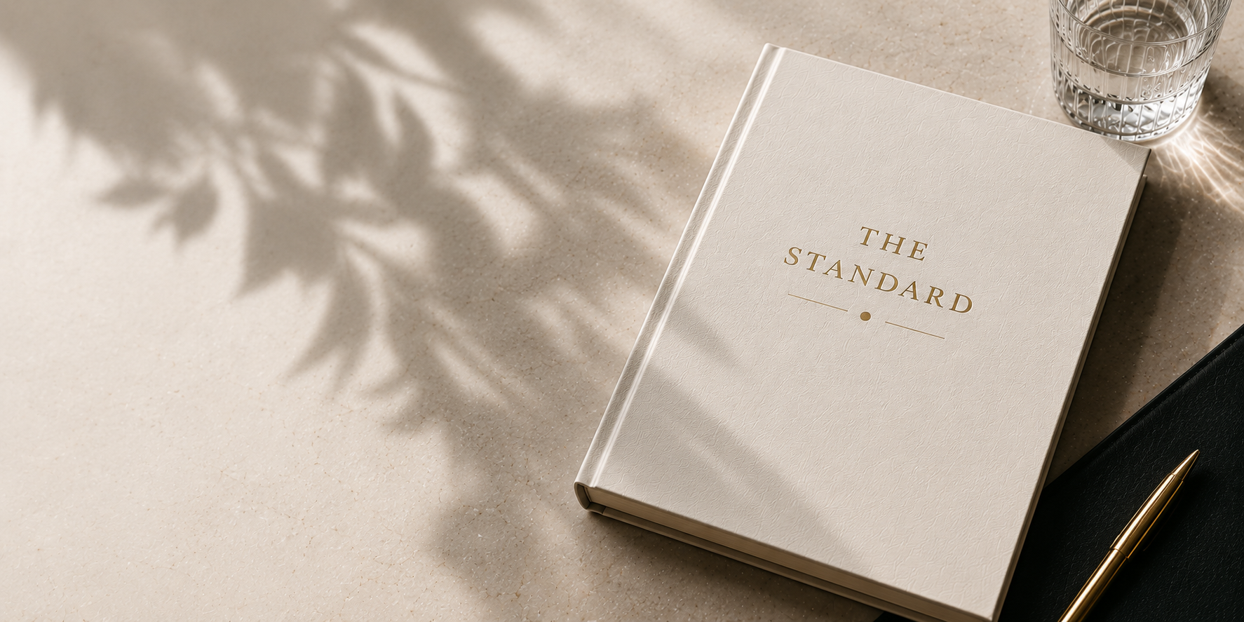 The Standard — a cream hardcover book on marble with a gold pen